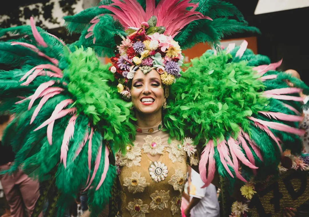 Smiling dancer in a green and pink feathered carnival costume with a flower headdress