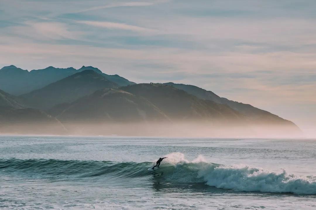 Surfer riding a wave with misty mountains behind
